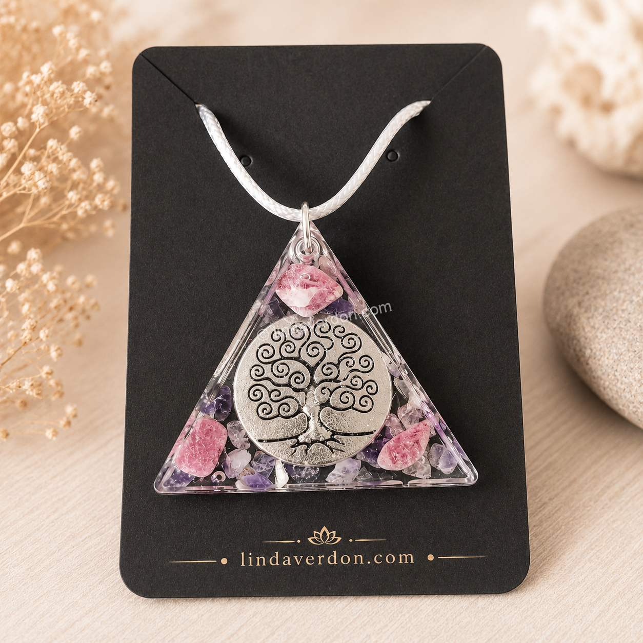 Découvrez ce Pendentif Arbre de Vie Rhodonite Améthyste, une création artisanale en résine époxy de forme triangulaire. Il associe la rhodonite, l'améthyste et le cristal de roche, sublimés par un magnifique Arbre de Vie argenté. Chaque création est préparée avec soin dans l'atelier Linda Verdon et livrée avec son cordon.