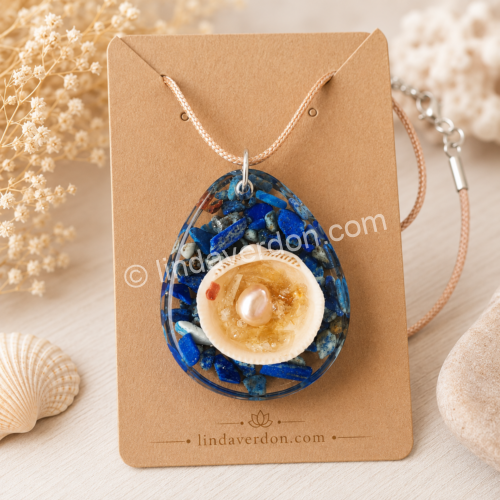 Découvrez ce pendentif artisanal en lapis-lazuli avec coquille d'eau, citrine et perle d'eau douce. Une création unique réalisée en résine époxy et préparée avec soin dans l'atelier Linda Verdon.