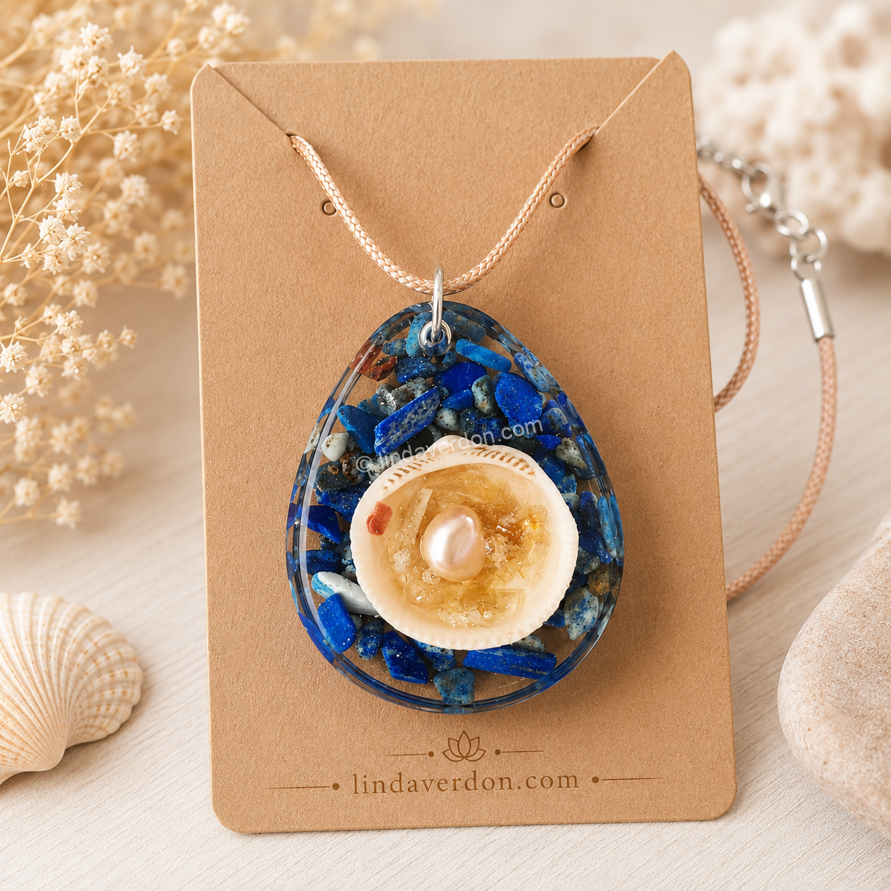 Découvrez ce pendentif artisanal en lapis-lazuli avec coquille d'eau, citrine et perle d'eau douce. Une création unique réalisée en résine époxy et préparée avec soin dans l'atelier Linda Verdon.
