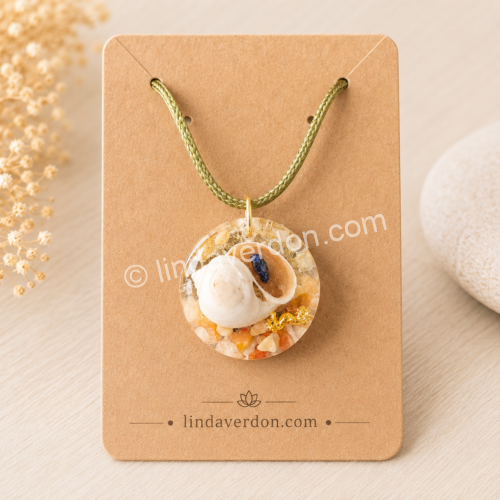 Découvrez ce pendentif artisanal en citrine, cristal de roche et coquillage naturel orné d'un éclat de lapis-lazuli. Une création unique réalisée en résine époxy et préparée avec soin dans l'atelier Linda Verdon.