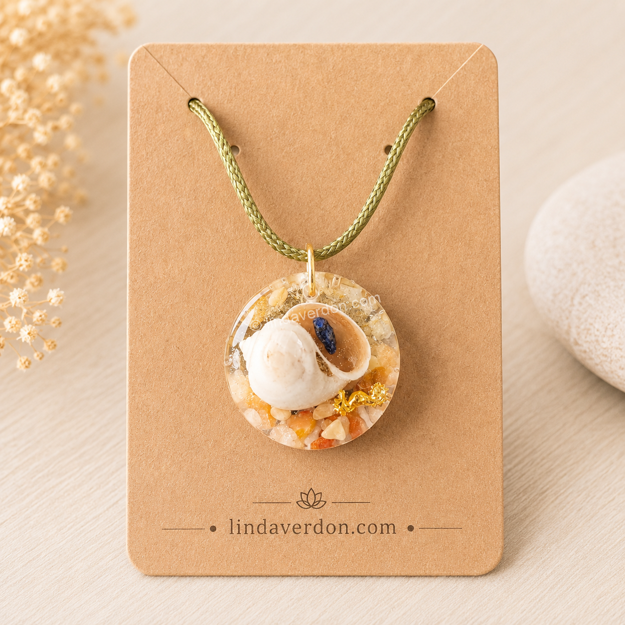 Découvrez ce pendentif artisanal en citrine, cristal de roche et coquillage naturel orné d'un éclat de lapis-lazuli. Une création unique réalisée en résine époxy et préparée avec soin dans l'atelier Linda Verdon.